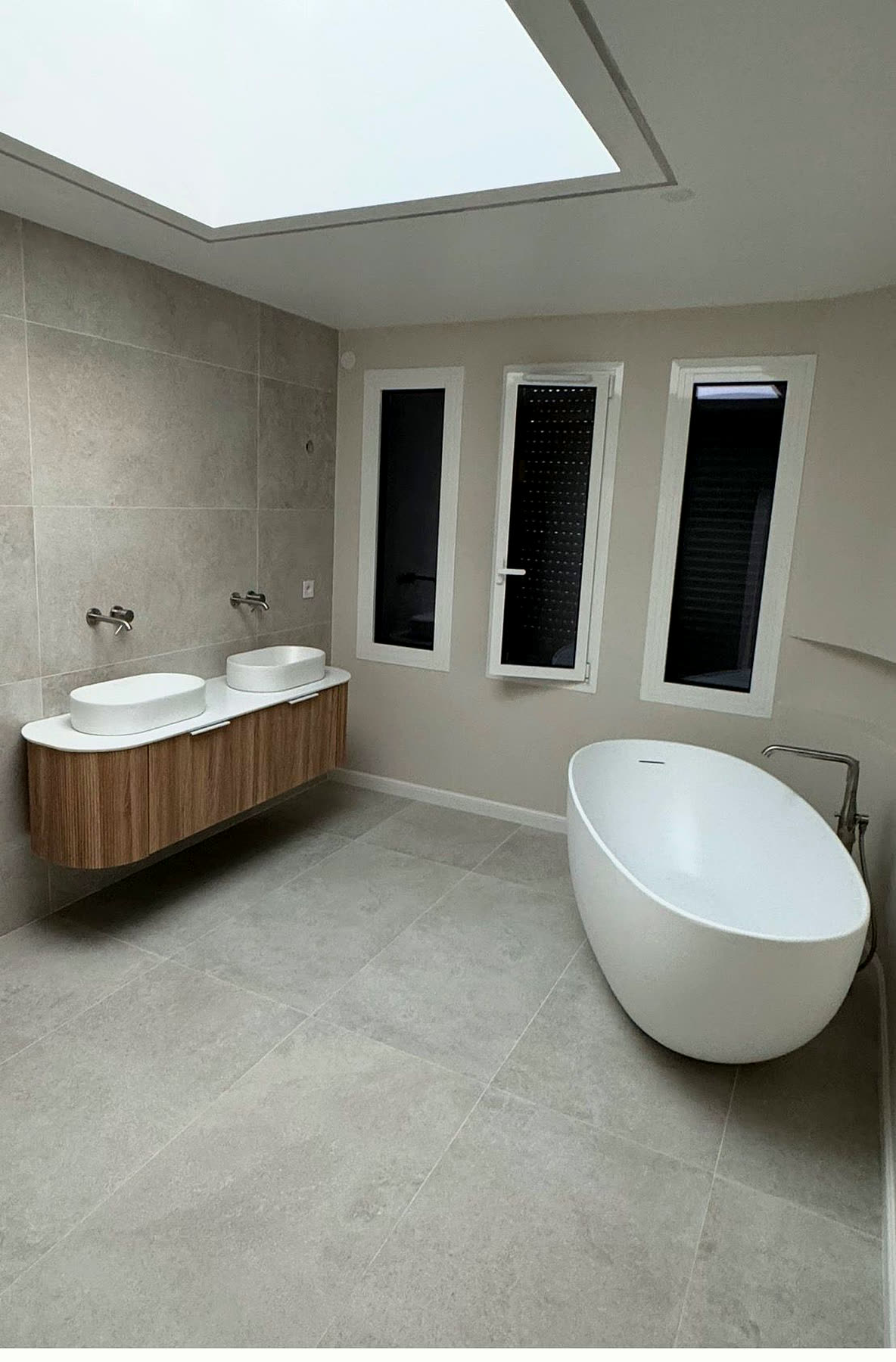 Salle de bain rénovée par Sani-Chauffe : meuble suspendu double vasque, baignoire îlot et grand format effet pierre